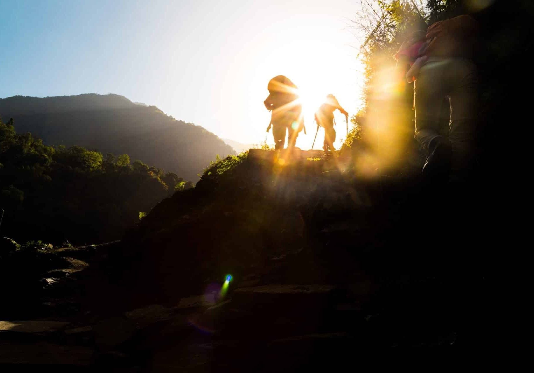 Female in silhouette hiking at highland towards sunrise. Lens flare intended